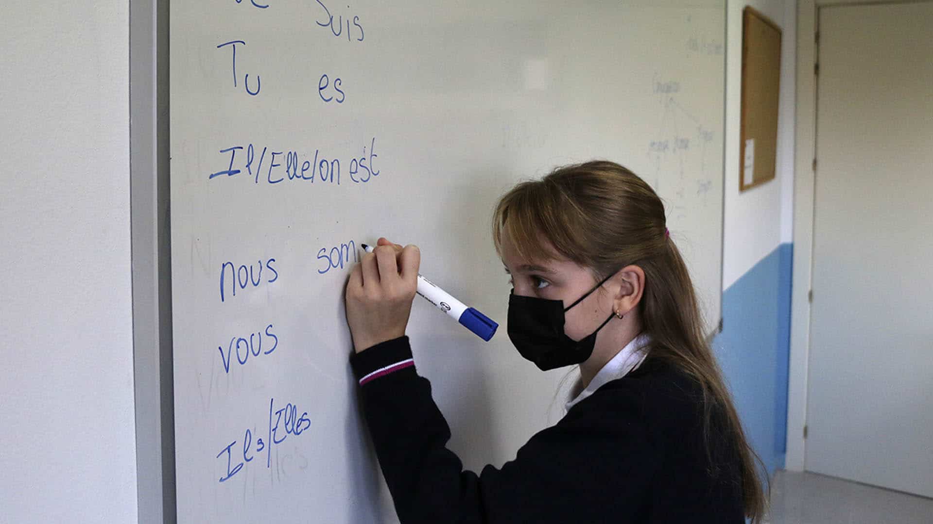 Alumna escribe el verbo être en la pizarra.
